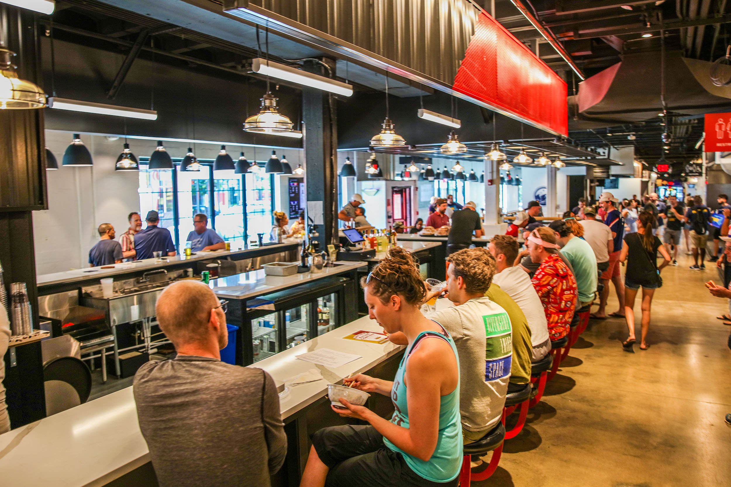 A lively food hall with diners gathering at a long bar